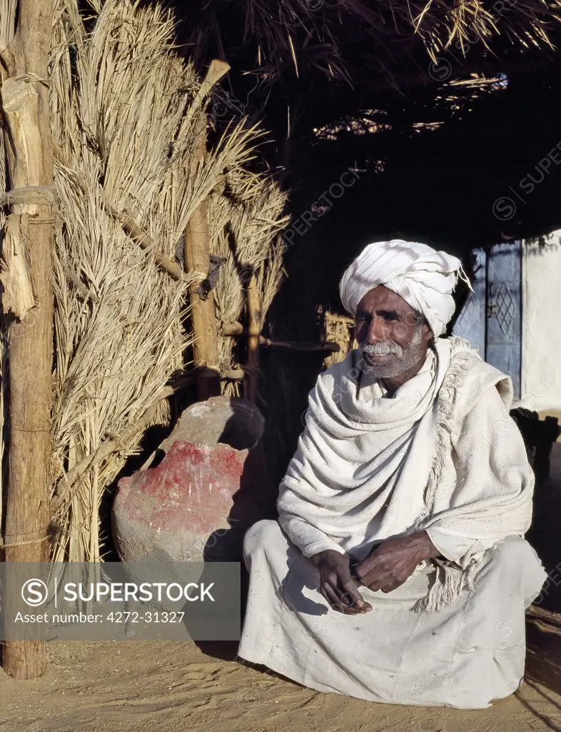 A Nubian man squats beside an old water container at an oasis in the Nubian Desert north of Old Dongola.