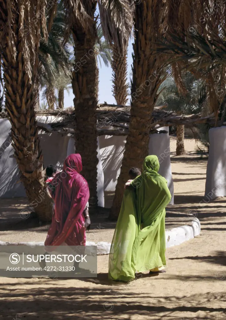 Nubian women in colourful attire walk beneath date palms at Old Dongola.