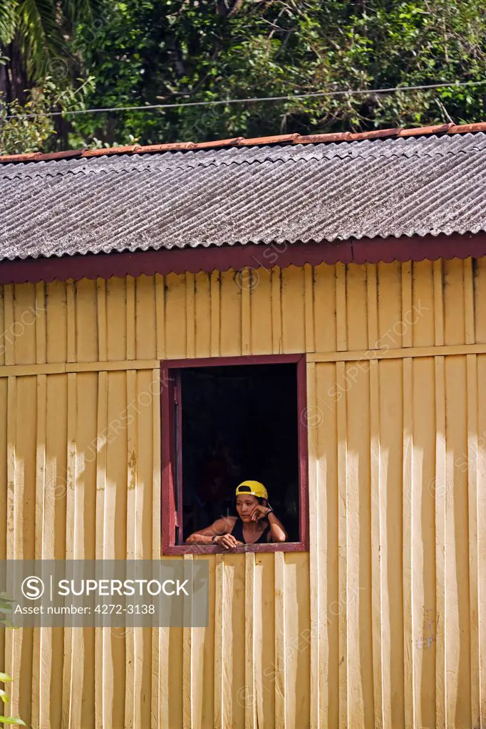 Brazil, Amazon, Rio Tapajos. A tributary of the Rio Tapajos which is itself a tributary of the Amazon. A woman in the village of Maguari watches life go by outside her window.