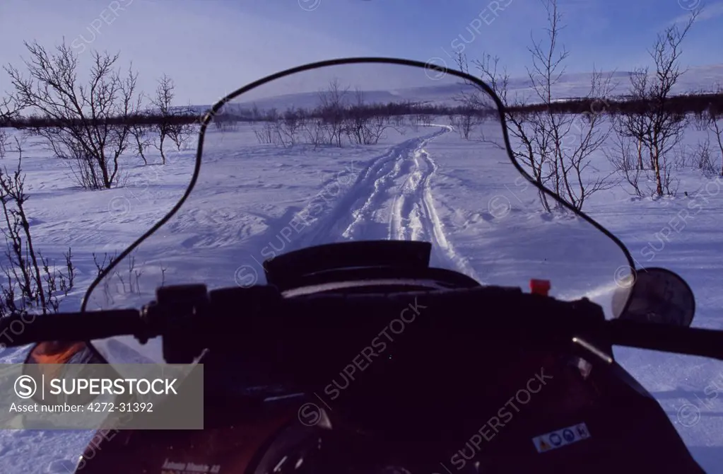 View over the front of a snowmobile on a trail through snow