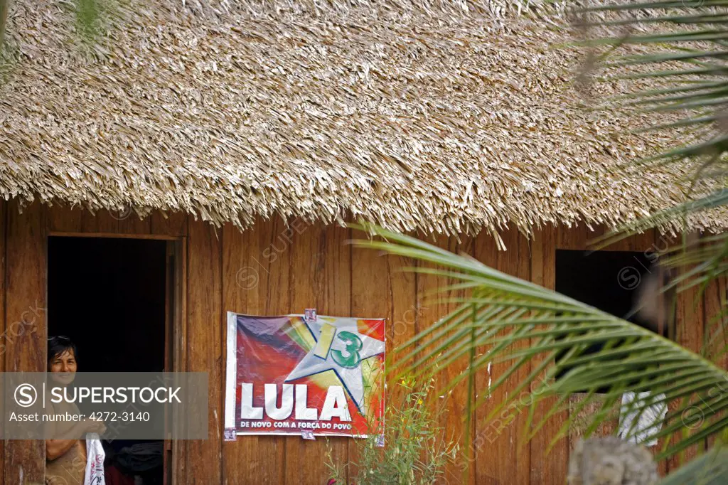 Brazil, Amazon, Rio Tapajos. A tributary of the Rio Tapajos which is itself a tributary of the Amazon. A lady looking out from her wooden house decorated with a political poster for senate candidate Lula in the village of Maguari.