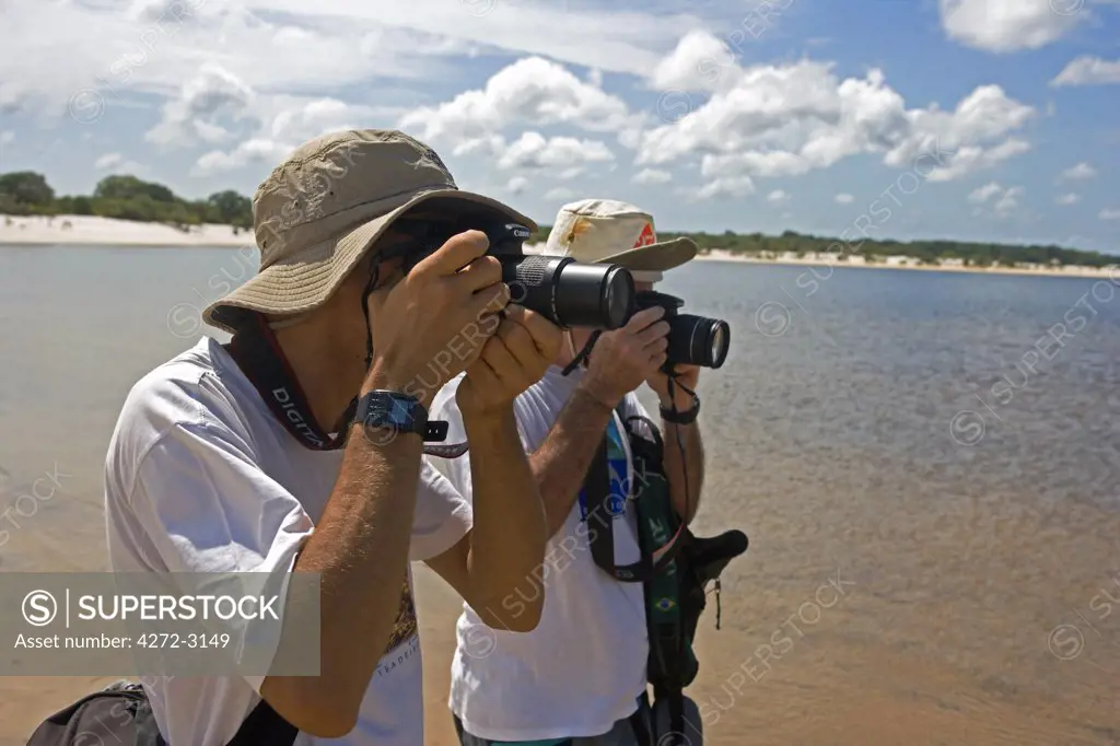 Brazil, Amazon, Rio Tapajos. A tributary of the Rio Tapajos which is itself a tributary of the Amazon is photographed by photographers trekking down its riverbank. (MR).