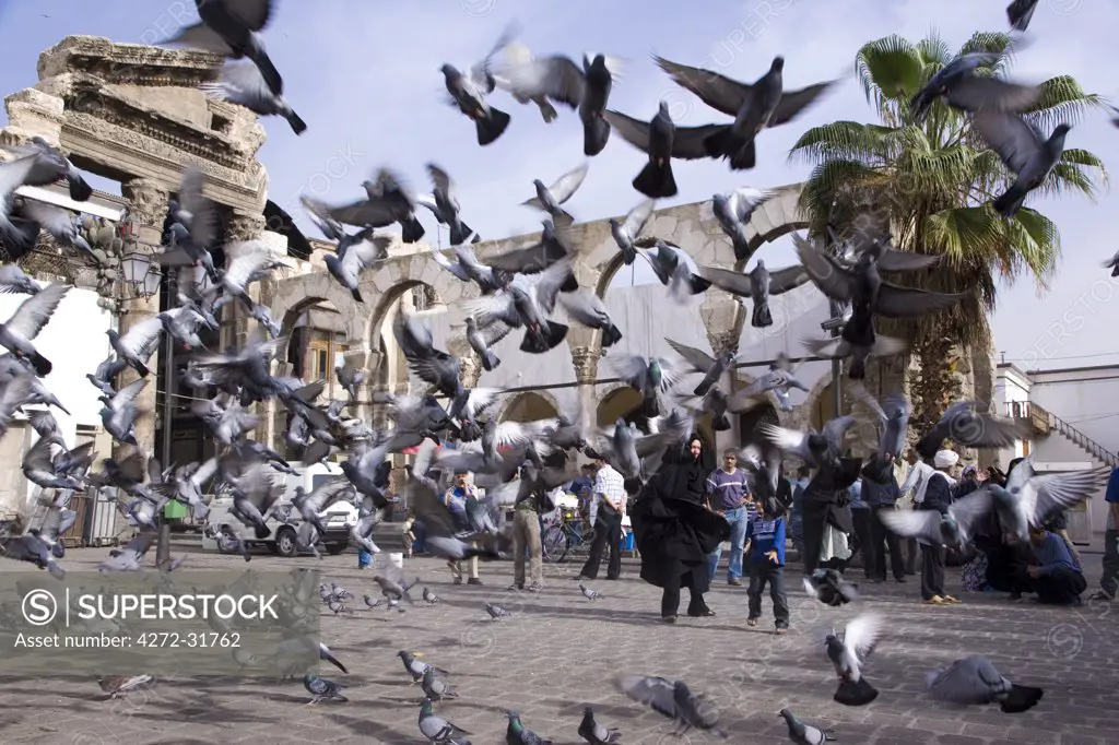 Feeding the pigeons in front of the remains of the Roman Western Temple Gate outside the Umayyad Mosque, Damascus, Syria