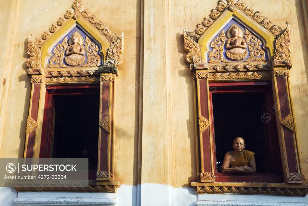 Thailand, Nong Khai, Nong Khai.  A monk looks out from a window at Wat Hai Sok.