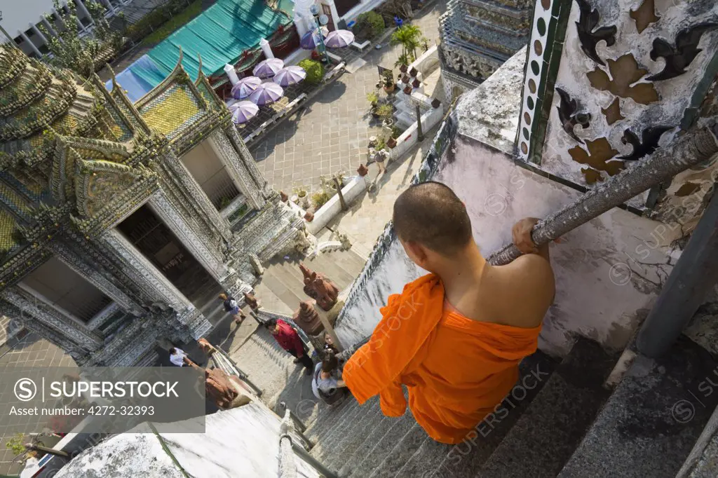 Thailand, Bangkok.  A monk descends the steps of the prang (Khmer-style tower) at Wat Arun.