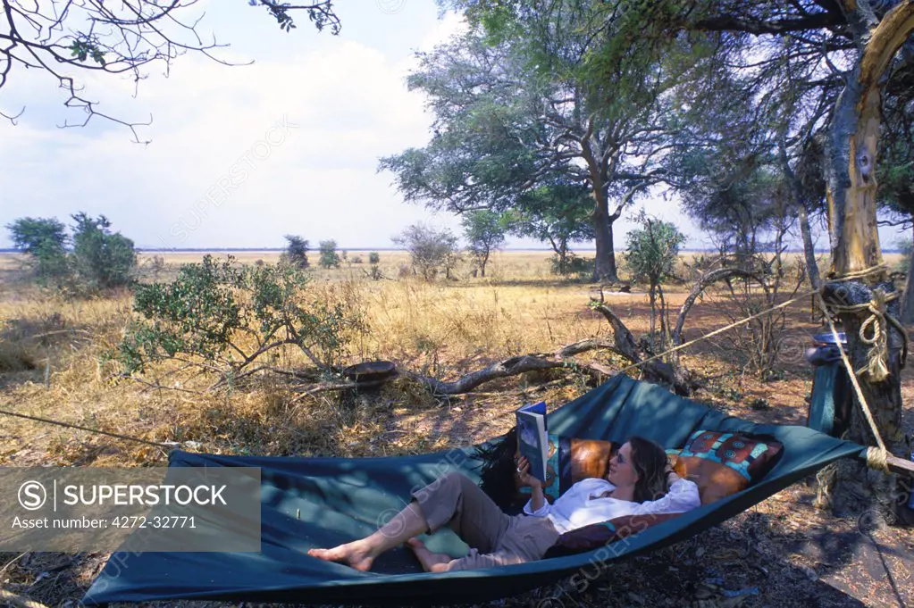 Tanzania, Katavi National Park. Relaxing reading a book in a hammock at Chada Camp.