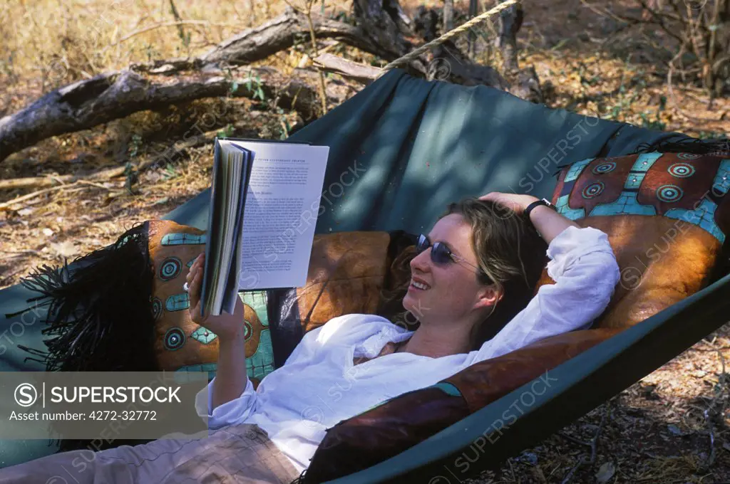 Tanzania, Katavi National Park. Relaxing reading a book in a hammock at Chada Camp.