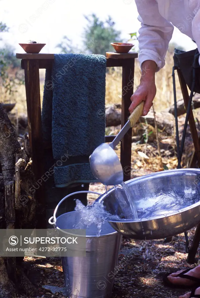 Tanzania, Katavi National Park.  Ladling water for washing into a bowl at Chada Camp.