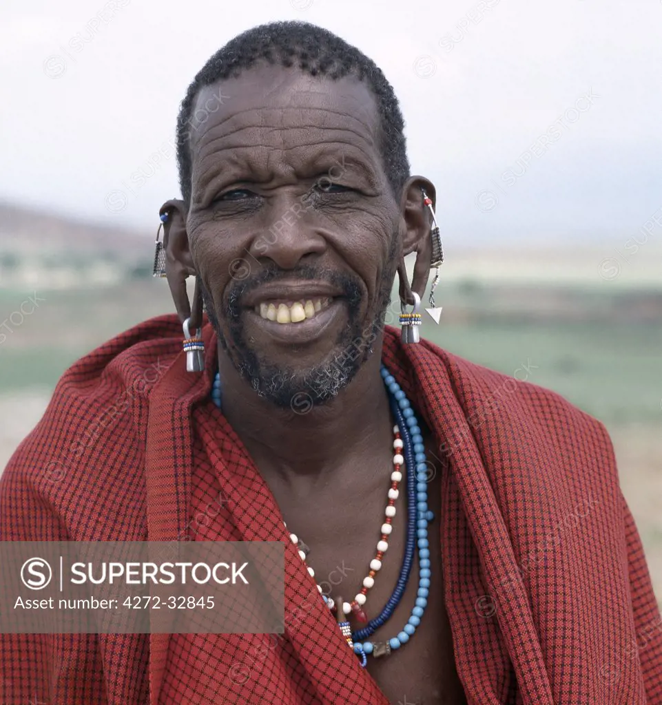 A Maasai elder in traditional attire.  Red has always been the preferred Maasai colour.  Bell-shaped brass earrings are typically worn by the elders of the tribe.