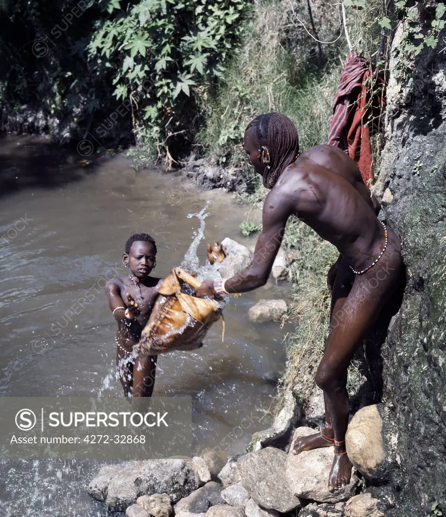 A Maasai warrior and a young herdsboy draw water for livestock from the deep wells at Naberera where cattle paths are cut deep into the soil to allow livestock nearer to the source of water.