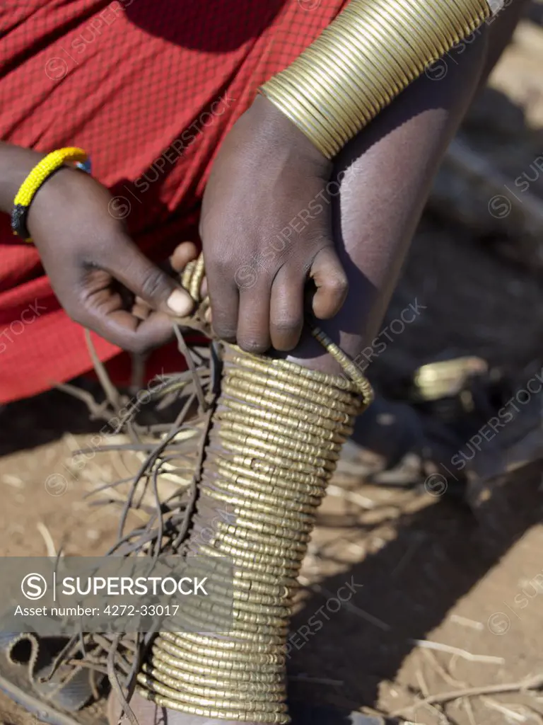 A Datoga woman puts on brass leg ornaments before attending a wedding. The traditional attire of Datoga women includes beautifully tanned and decorated leather dresses and coiled brass ornaments of every description. The Datoga live in northern Tanzania and are primarily pastoralists.
