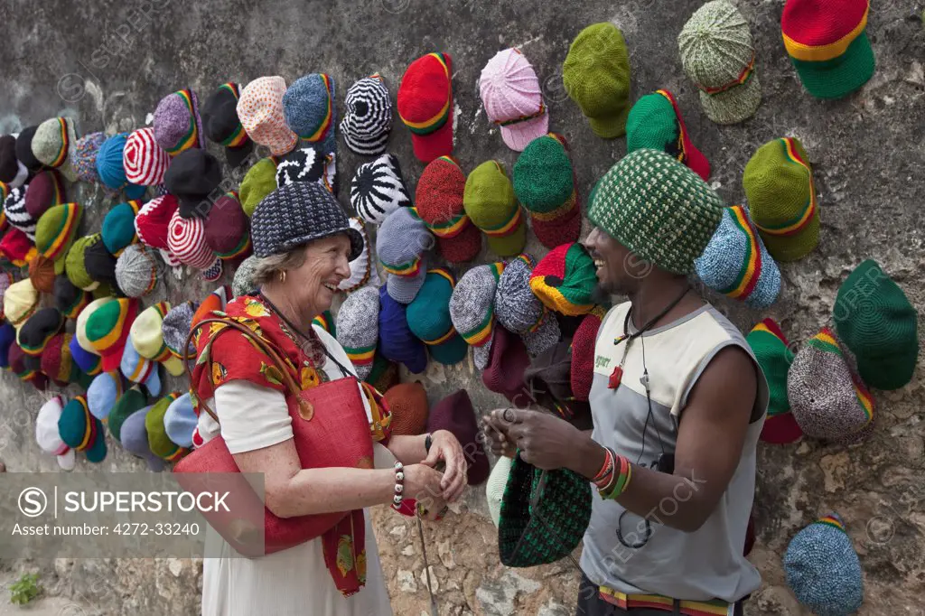 Tanzania, Zanzibar, Stone Town. An enterprising hat maker with an  eye-catching display on the wall of the old Omani Fort bargains with a  passing tourist. - SuperStock