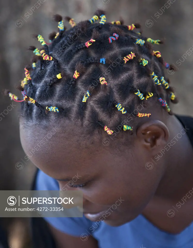 A young girl with a modern hairstyle using small coloured elastic bands to tie her braids.