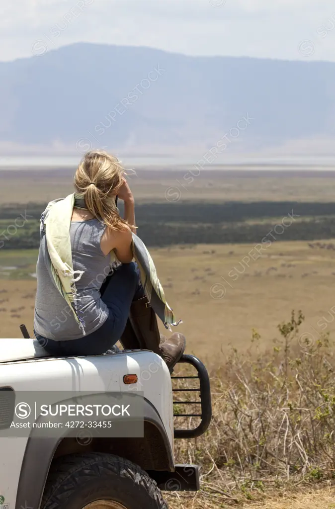 Tanzania, Ngorongoro. A tourist looks out over the Ngorongoro Crater from the bonnet of her Land Rover. MR.