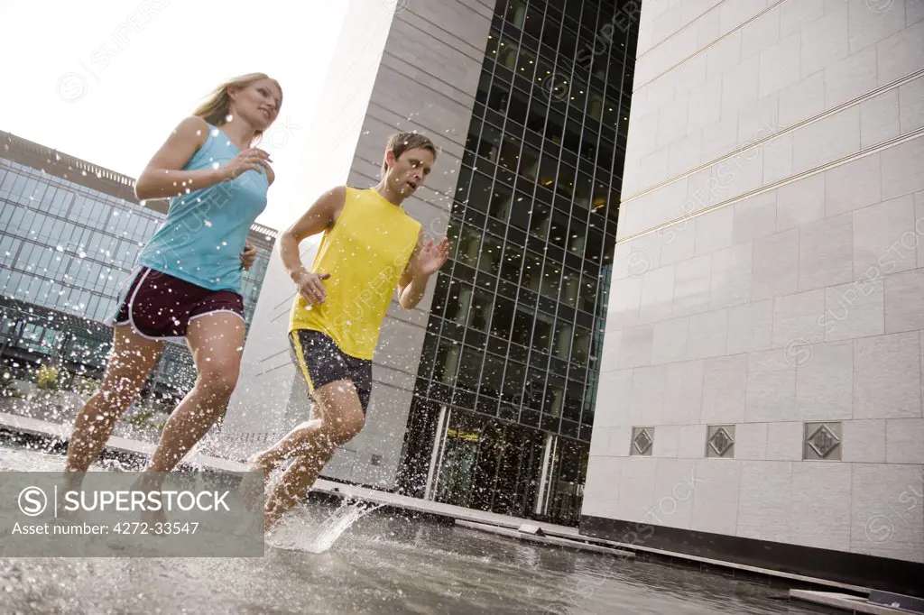 A man and woman running barefoot through water.