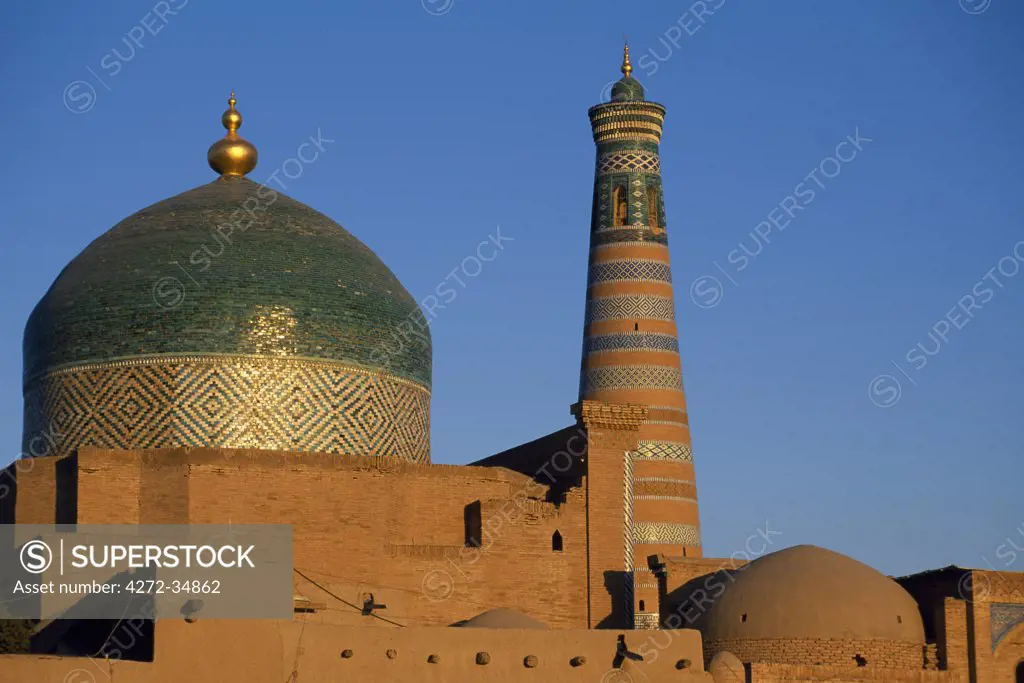 The minaret and tiled dome of a mosque rise above the old city of Khiva. The dome is covered in Khiva's hallmark green ceramic tiles.