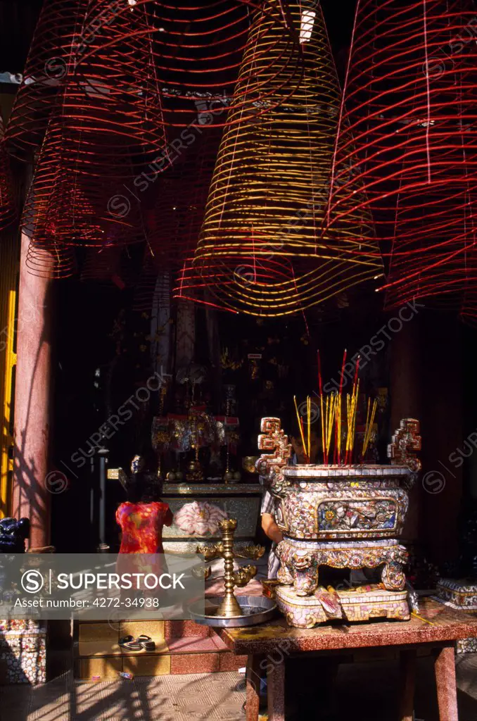 Woman praying at one of the shrines at Phoc An Hoi Quan Pagoda overlooked by coils of incense hanging from the roof interior .The Pagoda is surrounded by traditional turn-of-the-century Chinese merchant houses and dedicated to the Emperor Quan Cong.