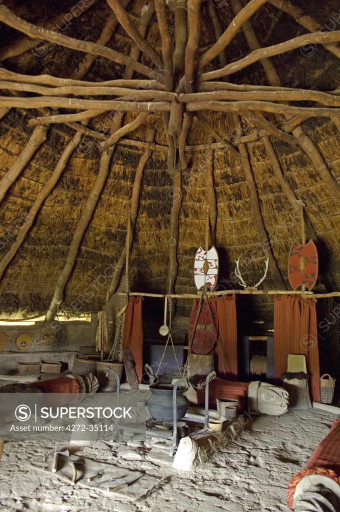 UK, Wales, Pembrokeshire. Interior of the re-created Chieftain's Hut, an Iron Age Celtic Roundhouse built on the original foundations , showing the fireplace, benches, sleeping area, thatched roof and wattle & daub walls at Castell Henlly, an Iron Age Fort near Newport.