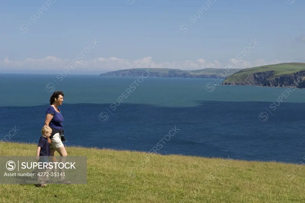 UK, Wales, Pembrokeshire. A mother walks with her young son along the Dinas Head section of the Pembrokeshire Coastal Path with views towards Newport Bay and the north Pembrokeshire coast beyond. (MR).