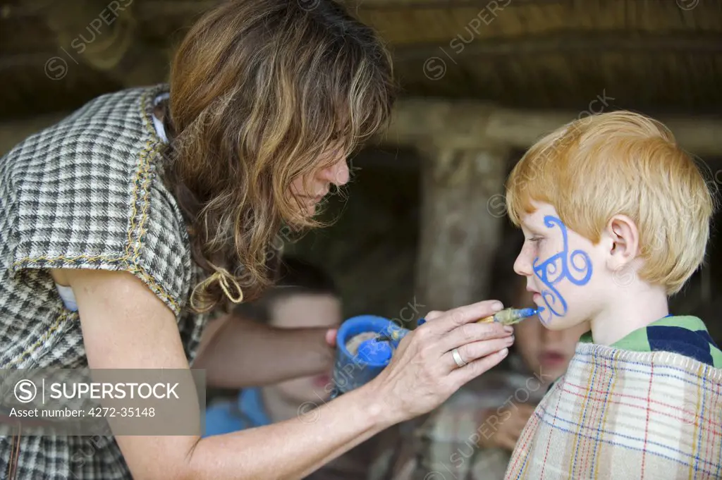 UK, Wales, Pembrokeshire. A young boy has his face painted with woad inn a Celtic symbol by one of the guides at Castle Henllys, a recreated Iron Age Fort built on its original foundations near Newport.