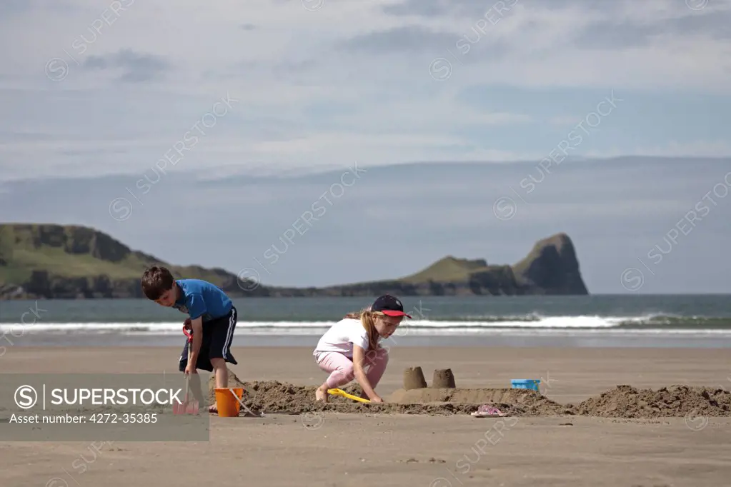 Wales, Gower. Children building sandcastles on the beach at Rhossili during low tide. (MR)