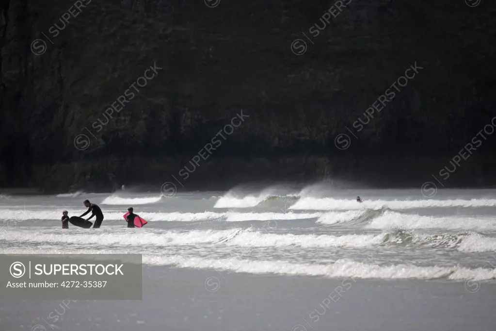 Wales, Gower. A father encourages his young children to go bodyboarding in the surf at Rhossili Bay.