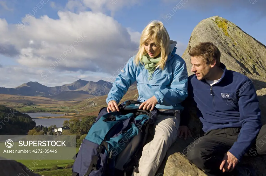North Wales, Snowdonia.  Man and woman sitting on rocks against the backdrop of Mt Snowdon. (MR)