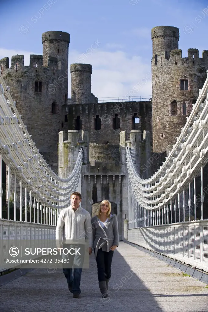 UK, North Wales; Conwy. Couple on the  elegant Suspension Bridge built by Thomas Telford across the Conwy River to the imposing Castle.  (MR)