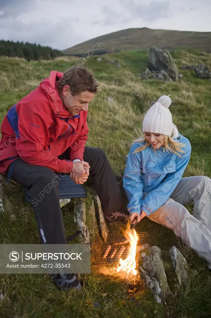 Gilar Farm, Snowdonia, North Wales.  Man and woman cooking over an open fire whilst camping in the wild. (MR)