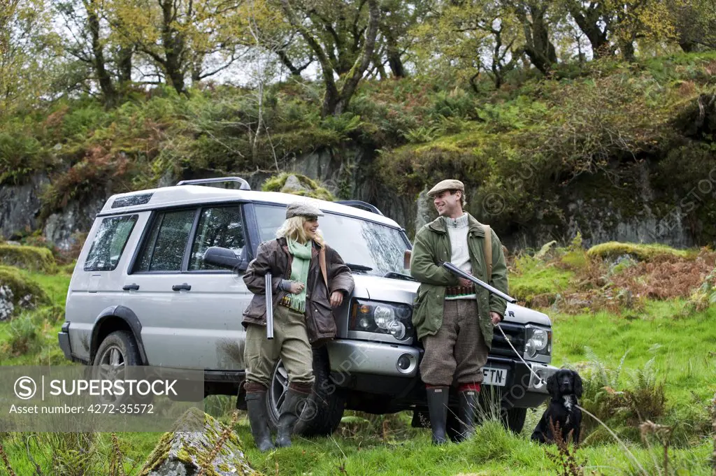 North Wales, Snowdonia ; Gilar Farm. A man and woman relax leaning against their landrover whilst out shooting. (MR)