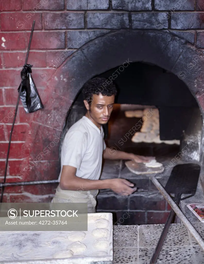 A man prepares to bake bread in a large oven in the market in old Sanaa.  Surrounded by a massive 20 to 30 foot high wall, old Sanaa is one of the worlds oldest inhabited cities. The suq or central market is located in a labyrinth of alleyways in the centre of the old city.