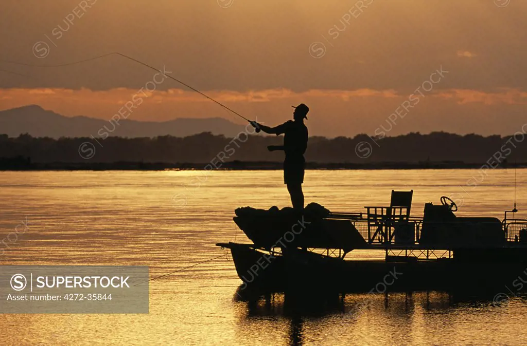 Zambia, Lower Zambezi National Park. Fly fishing for Tiger fish from a barge on the Zambezi River at dawn.