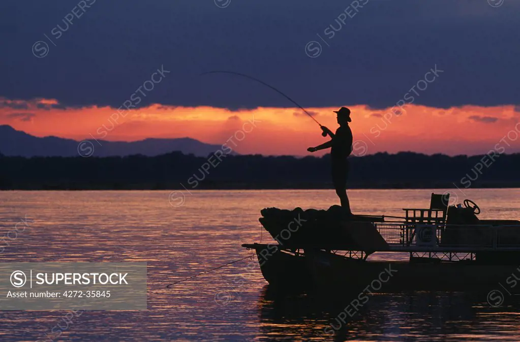 Zambia, Lower Zambezi National Park. Fly fishing for Tiger fish from a barge on the Zambezi River at dawn.