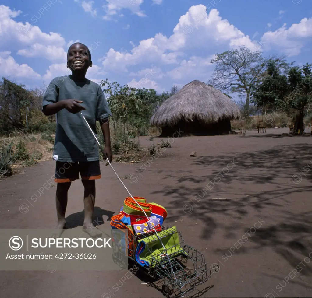 Range of fabrics designed and manufactured in the Luangwa Valley by Tribal Textiles displayed by small boy with toy car.