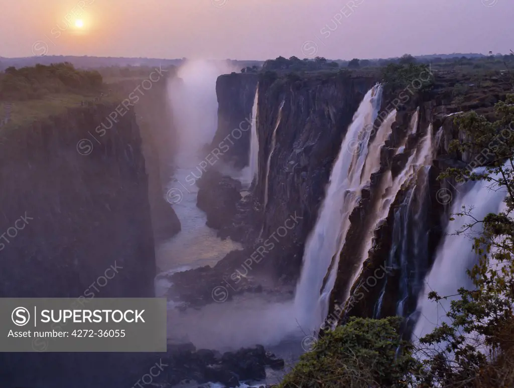 Sunset over the magnificent Victoria Falls. The Falls are more than a mile wide and are one of the world's greatest natural wonders. The mighty Zambezi River drops over 300 feet in a thunderous roar with clouds of spray