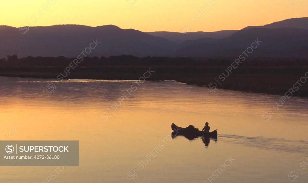 John Stevens paddling canoe on Zambezi from mana Pools, with Zambia in background.