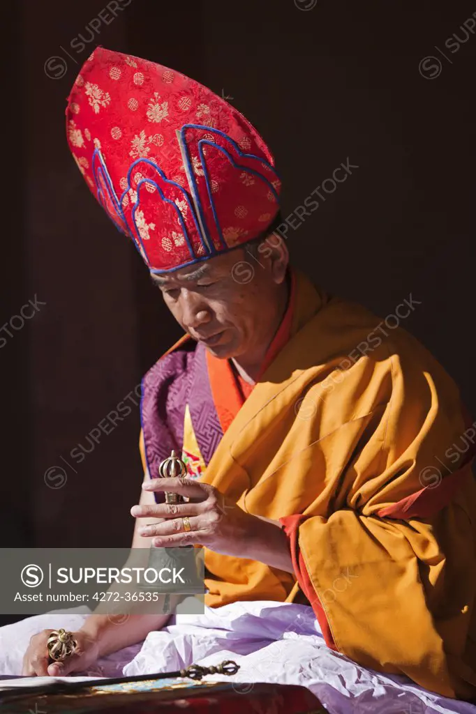 A senior monk conducting a puja at Gangtey Goemba, holding a vajra in one hand and ceremonial hand-bell in the other.