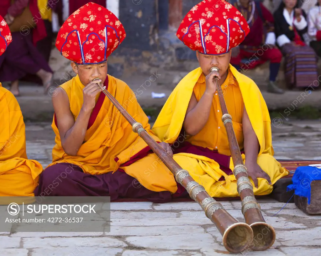 Monks in ceremonial robes blowing horns at a puja within Gangtey Goemba.