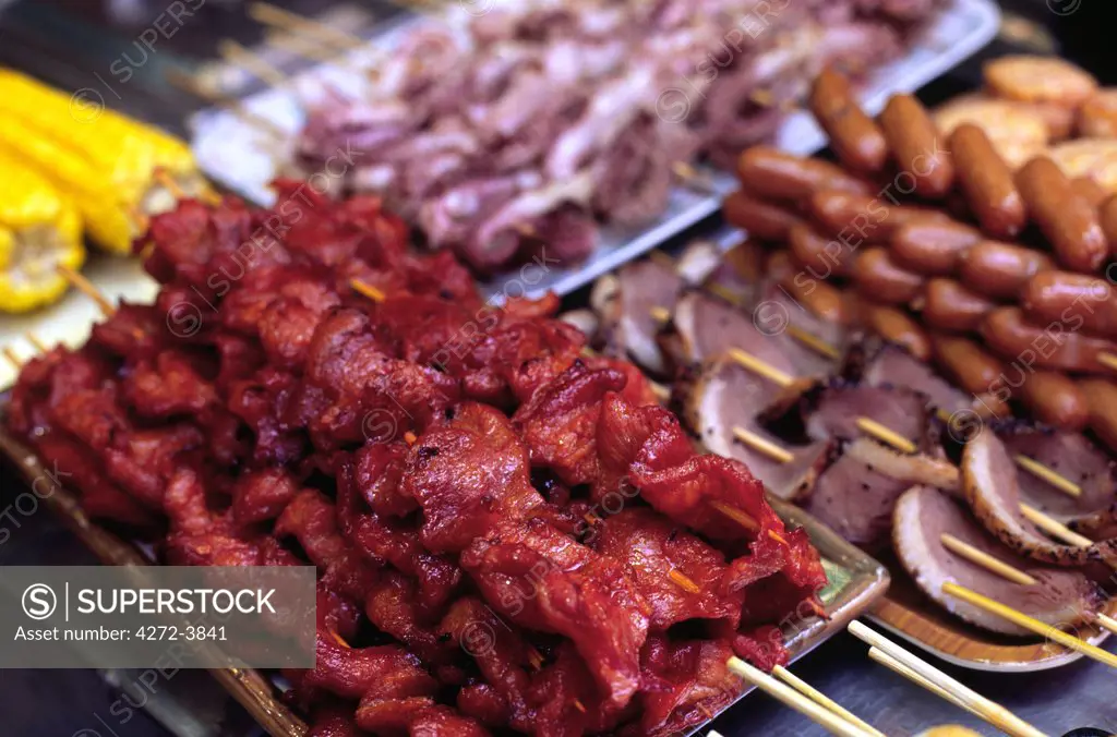 Barbeque pork skewers sit amongst trays of tasty snacks sold at a street stall in the Mong Kong district of Kowloon, Hong Kong