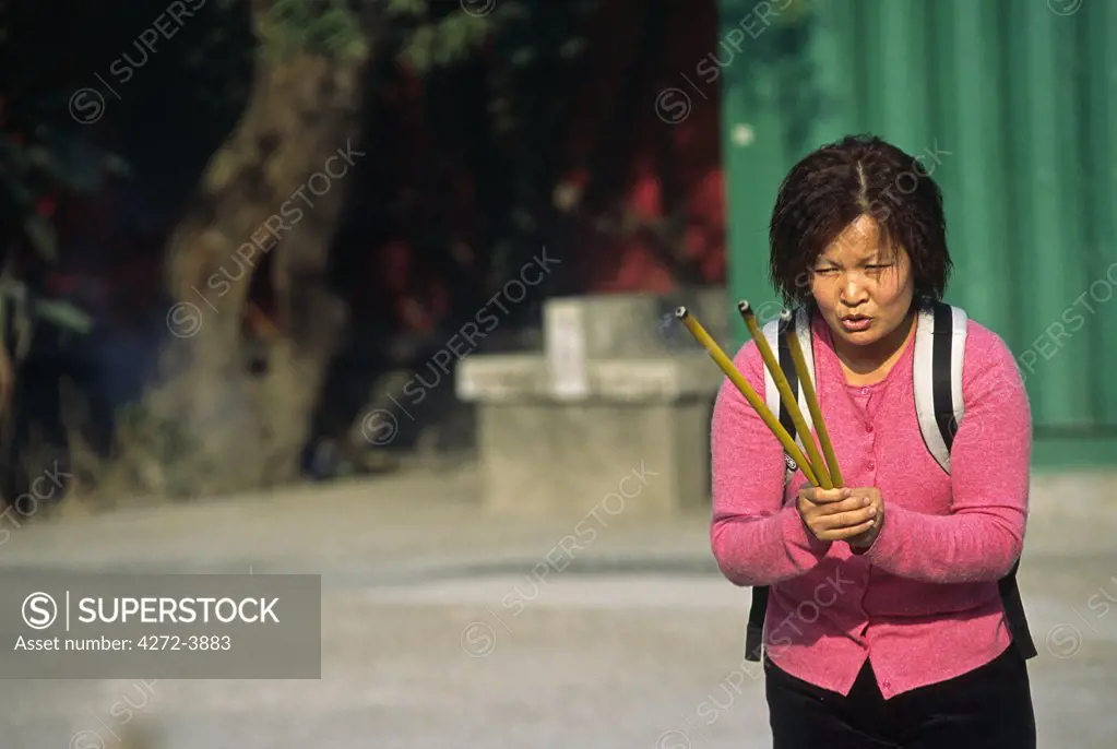 A woman offers incense at the foot of the Tian Tan Buddha on Lantau Island, Hong Kong.