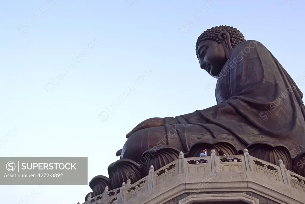 A pilgrim is dwarfed by the giant Tian Tan Buddha, a bronze, seated representation of Lord Gautama, sitting above Ngong Ping on Lantau Island, Hong Kong.
