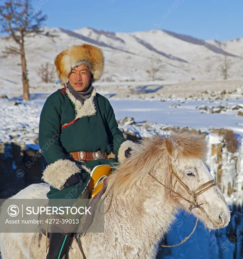 Mongolia, Ovorkhangai, Orkkhon Valley. A man sits on horseback by a frozen waterfall on the Orkhon River.