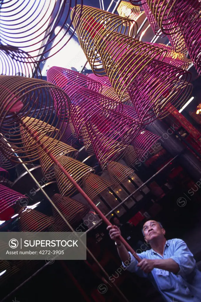 A caretaker raises incense coils suspended from the ceiling of the Man Mo Temple in Shueng Wan district on Hong Kong Island. The incense spirals are burnt as offerings by the worshippers.
