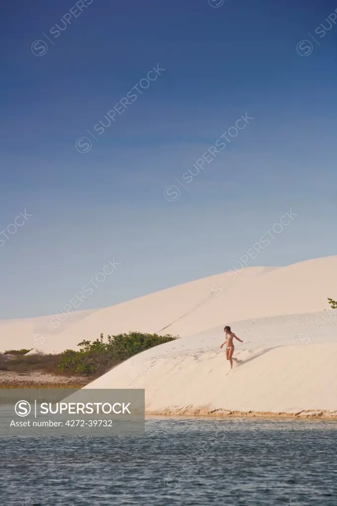 South America, Brazil, Maranhao, a woman in a bikini descends a dune in the Lagoa do Peixe in the Lencois Maranhenses