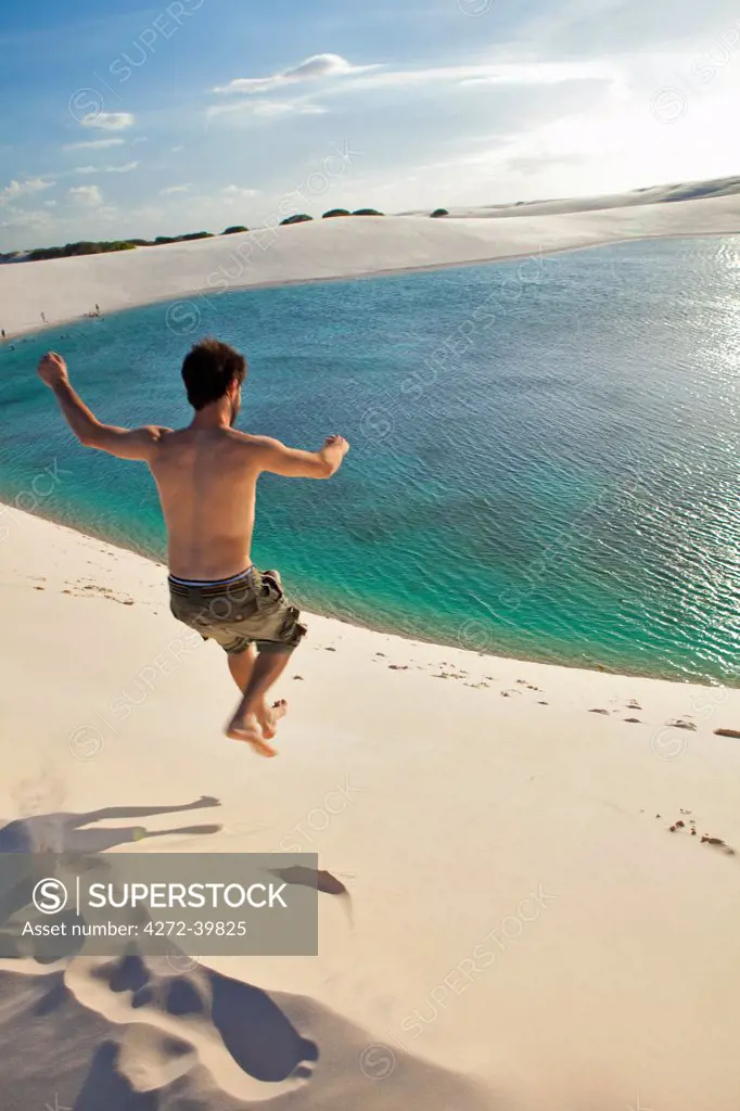 South America, Brazil, Maranhao, a man jumps off a dune into a green lake in the Lencois Maranhenses