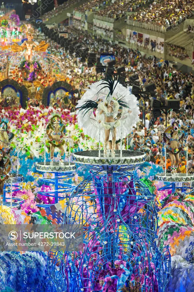 South America, Rio de Janeiro, Rio de Janeiro city, costumed dancer in a feather headdress and the floats and dancers of the Caprichosos samba school at carnival in the Sambadrome Marques de Sapucai