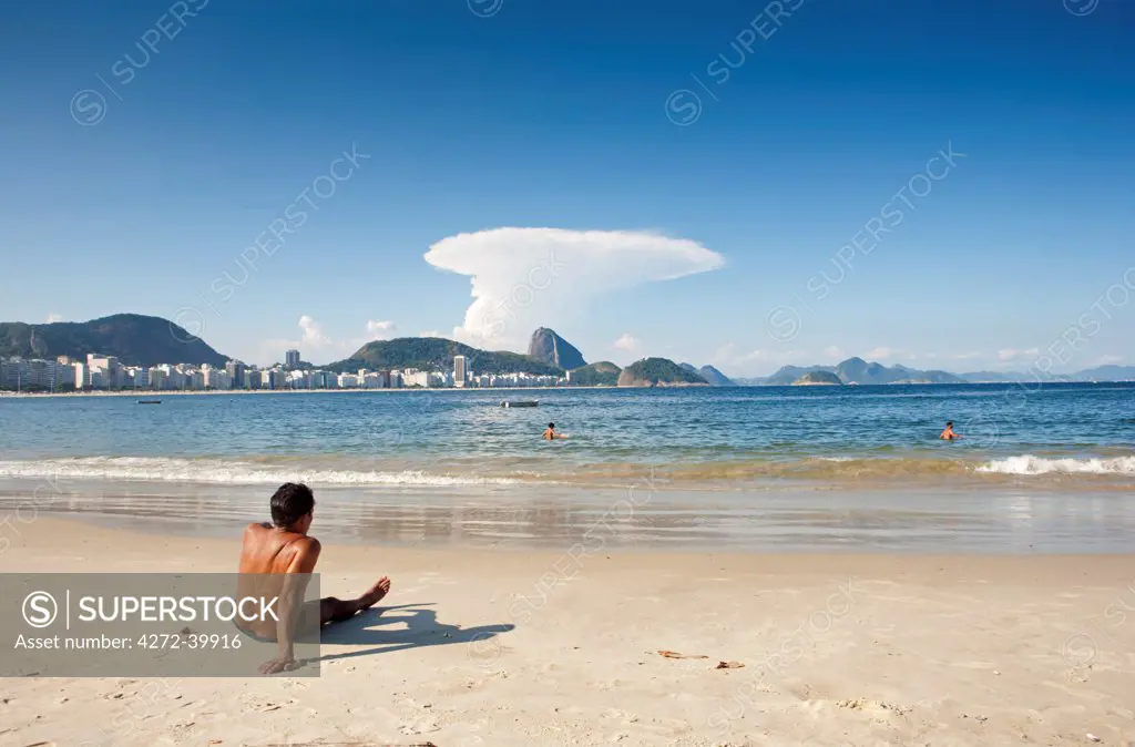 South America, Rio de Janeiro, Rio de Janeiro city, a sunbather at the end of Copacabana Beach with Copacabana and the Morro do Leme hill in the background