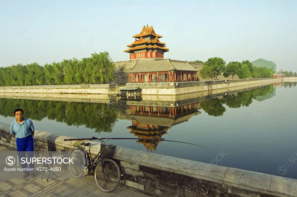 A man fishing in the moat with a reflection of the Palace Wall Tower of The Forbidden City Palace Museum, Zijin Cheng, Beijing, China