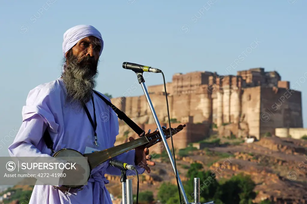 India, Rajasthan, Jodhpur. Framed by the massive Mehrangarh Fort, Khaibar Fakir, a Baul musician plays a dotara at the 2010 Rajasthan International Folk Festival