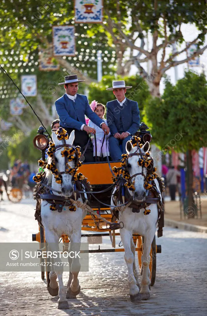 Seville, Andalusia, Spain, Two men and a girl in traditional clothes on a carriage drawn by horses at the Feria de Abril